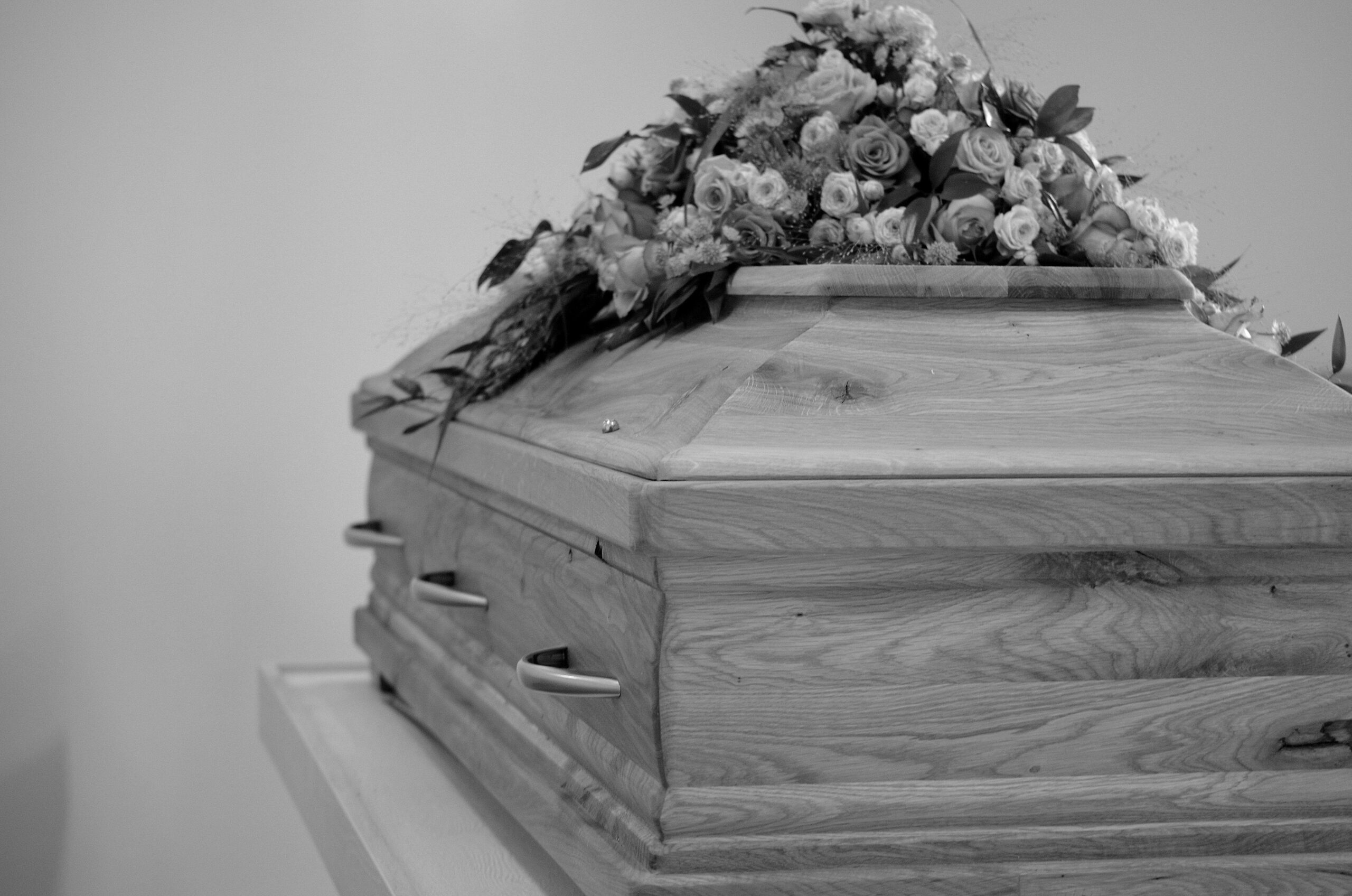 Black and white photo of a wooden coffin adorned with a detailed floral arrangement.